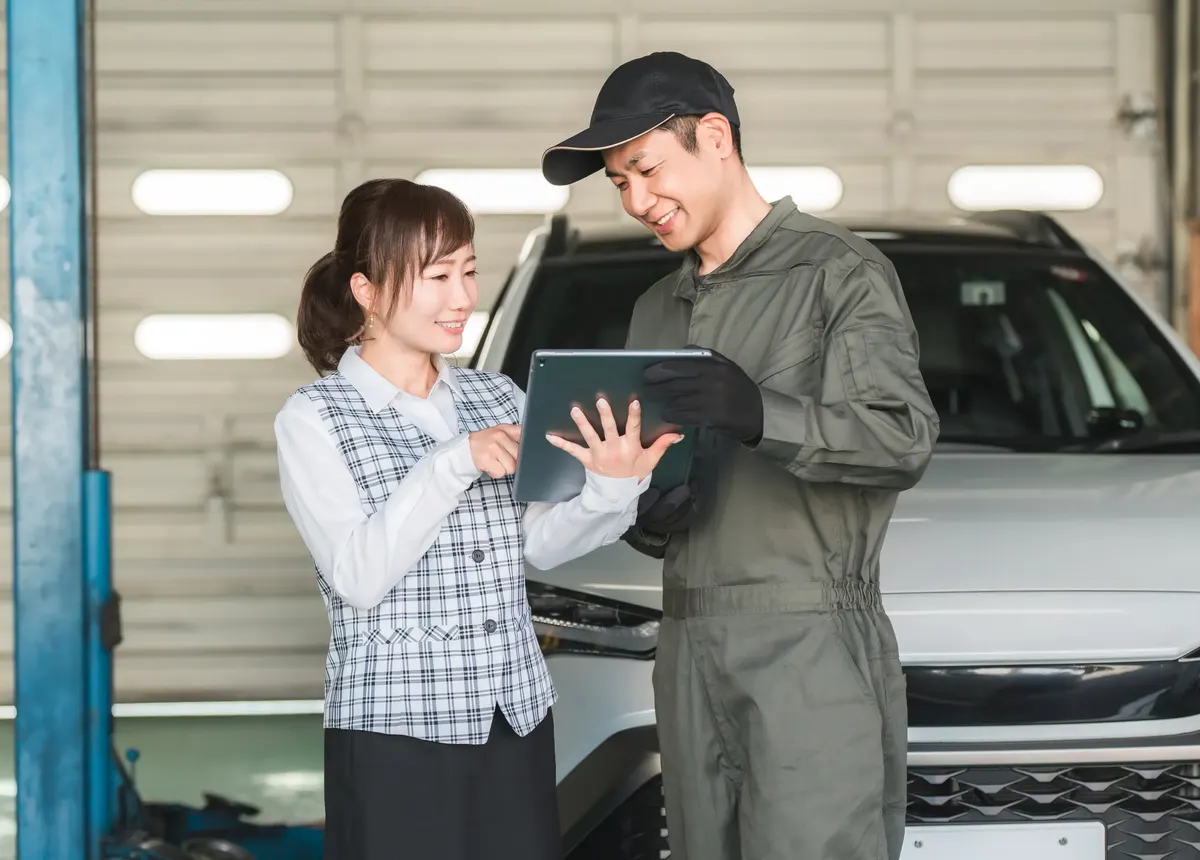 整備工場でタブレットを確認する整備士と受付担当